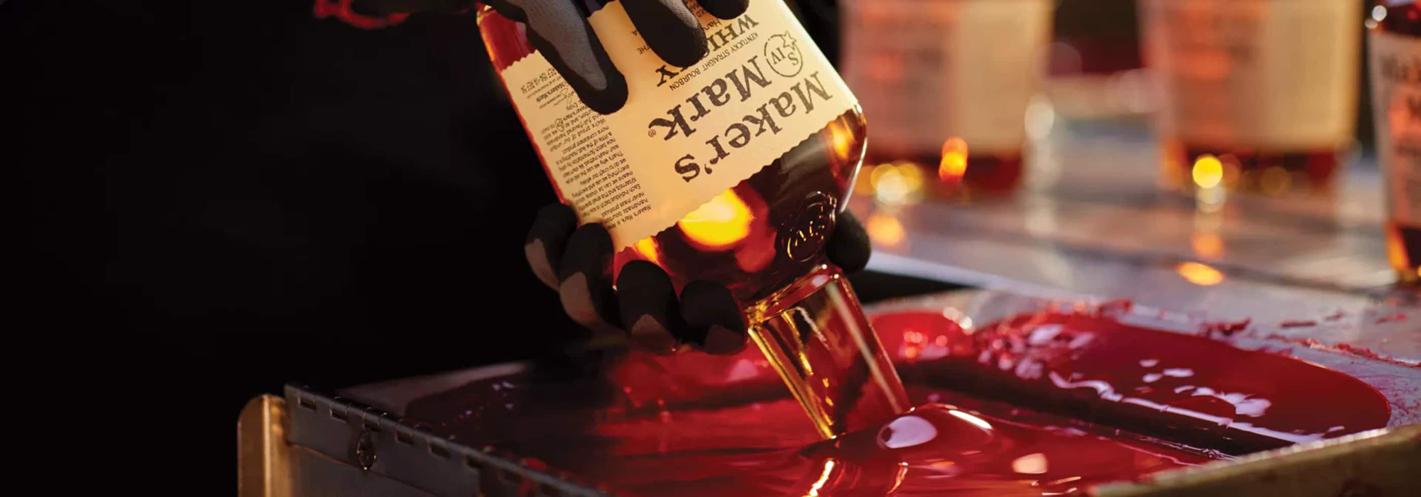 A bottle of Maker's Mark is dipped into a vat of the iconic red wax that seals the bottle